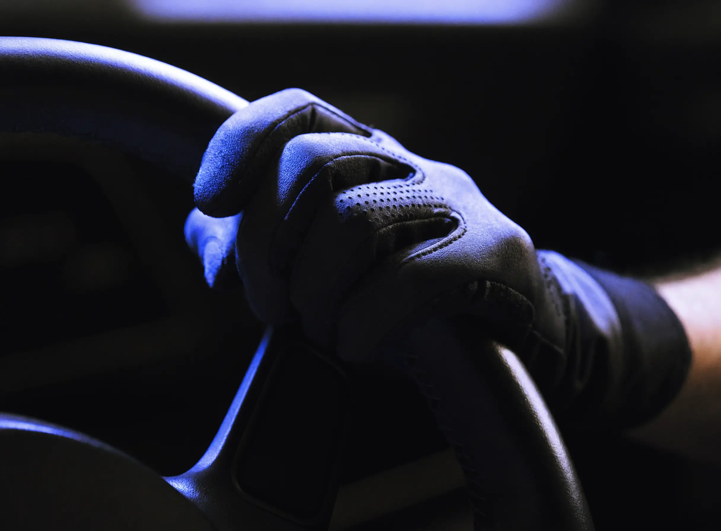 A racing-gloved hand gripping a steering wheel under blue light