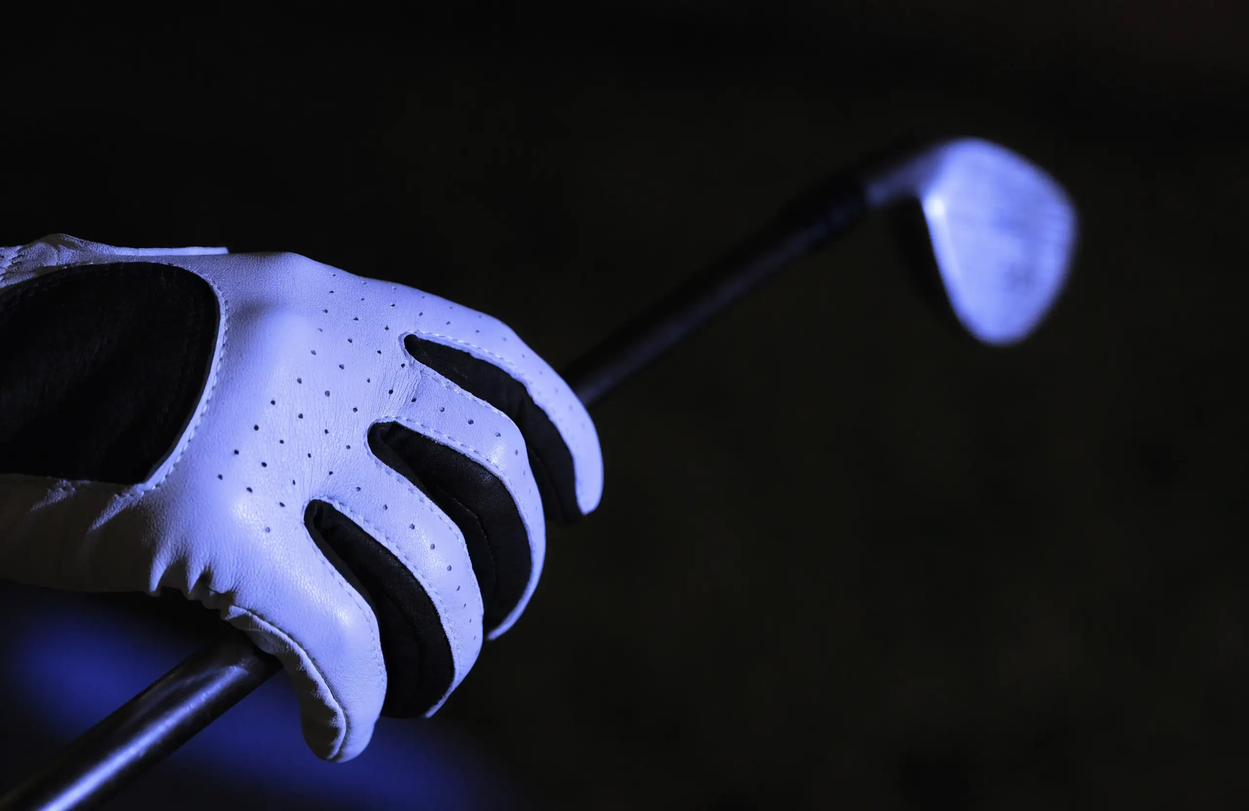 Golfer wearing a performance glove, mid-swing on a course at dusk