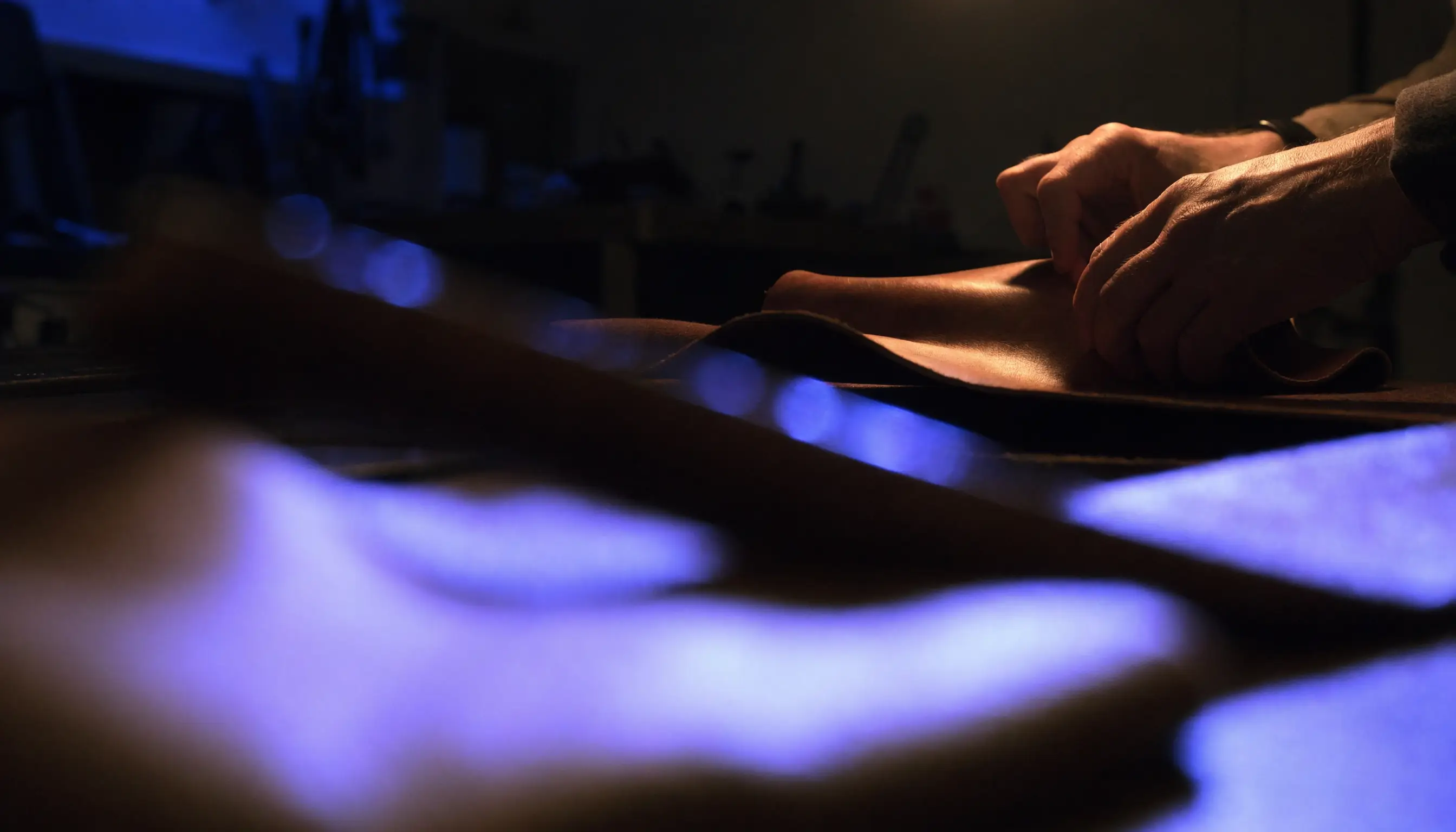 A craftsperson's hands working leather at a workshop bench