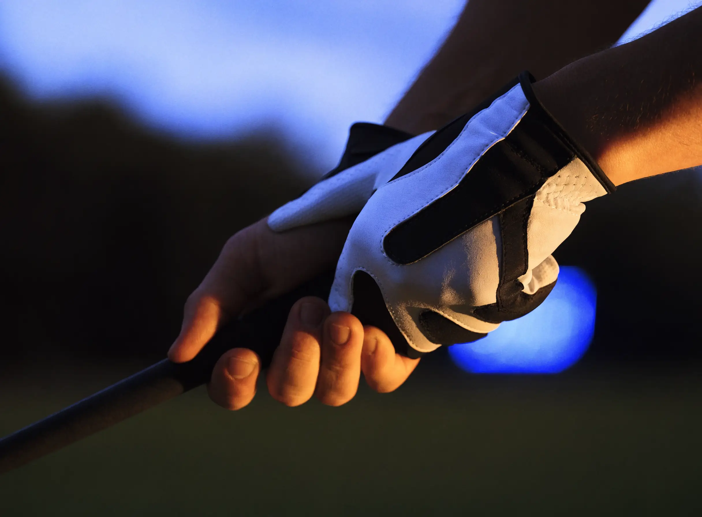 Gloved hands gripping a golf club at dusk