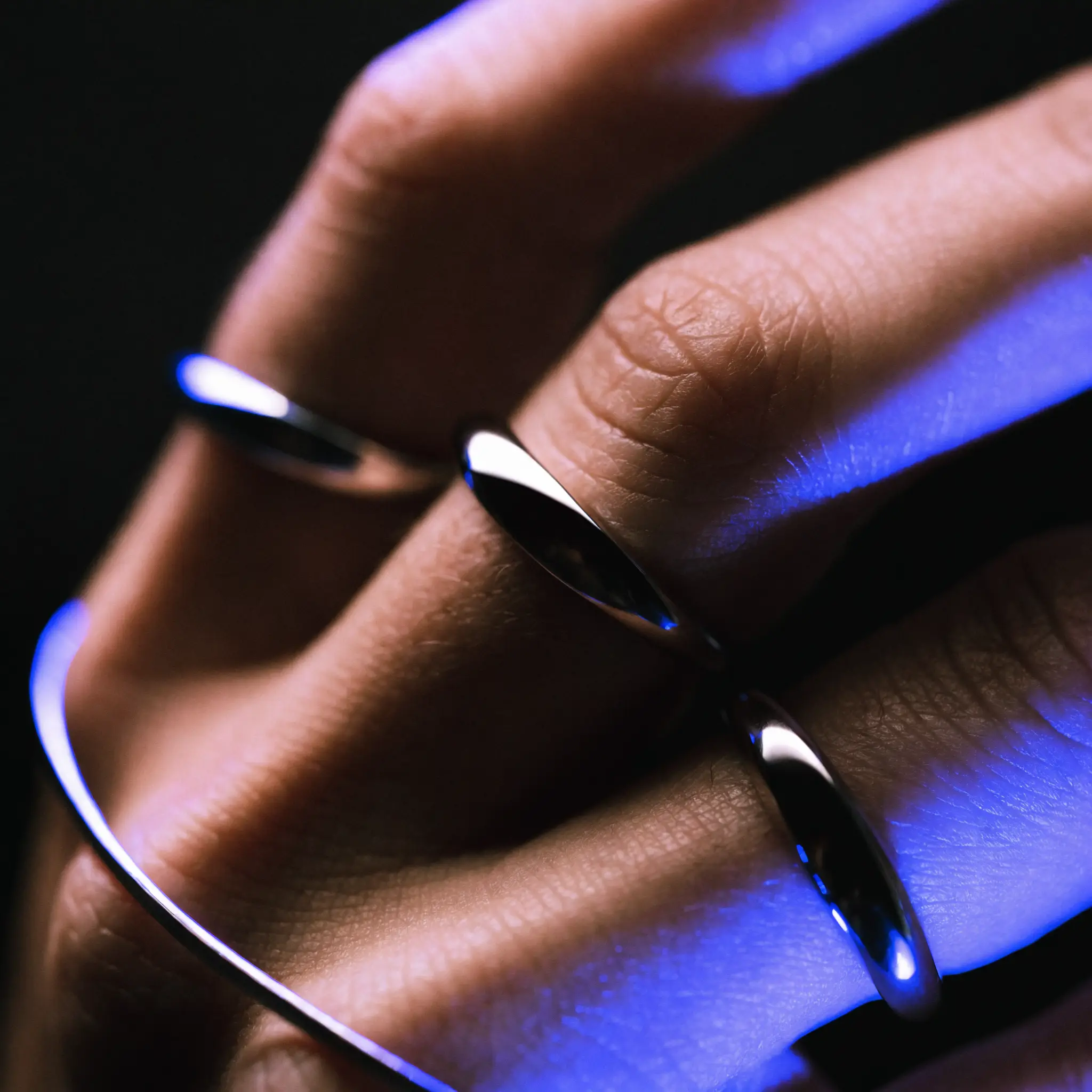 A hand wearing premium rings under blue rim light
